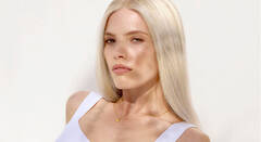 A person with sleek, straight blonde hair wearing a white outfit and a gold necklace.