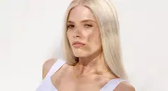 A person with sleek, straight blonde hair wearing a white outfit and a gold necklace.